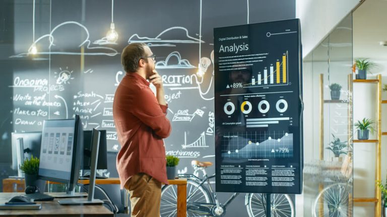 Male digital marketer looking at an interactive touchscreen in an office after completing his digital marketing diploma